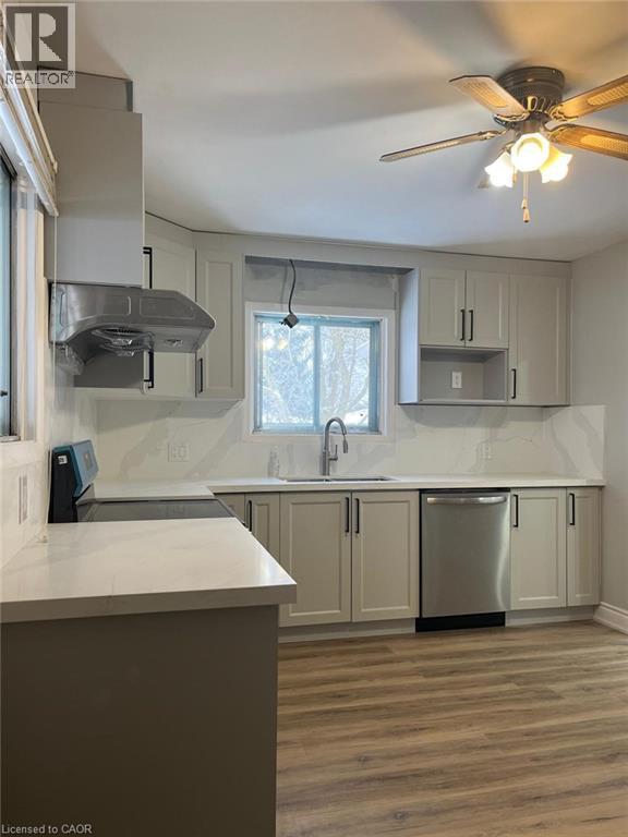 Kitchen featuring light-toned cabinetry, light-toned countertops, a stainless steel range hood, a stainless steel sink with a gooseneck faucet, and wood-finish flooring - 102 Massey Avenue, Kitchener, ON