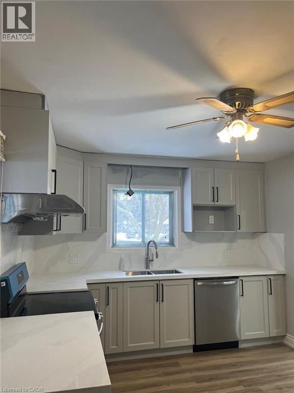 Kitchen featuring light gray cabinetry, white countertops, stainless steel appliances, a double basin sink with a gooseneck faucet, and wood-finish flooring - 102 Massey Avenue, Kitchener, ON