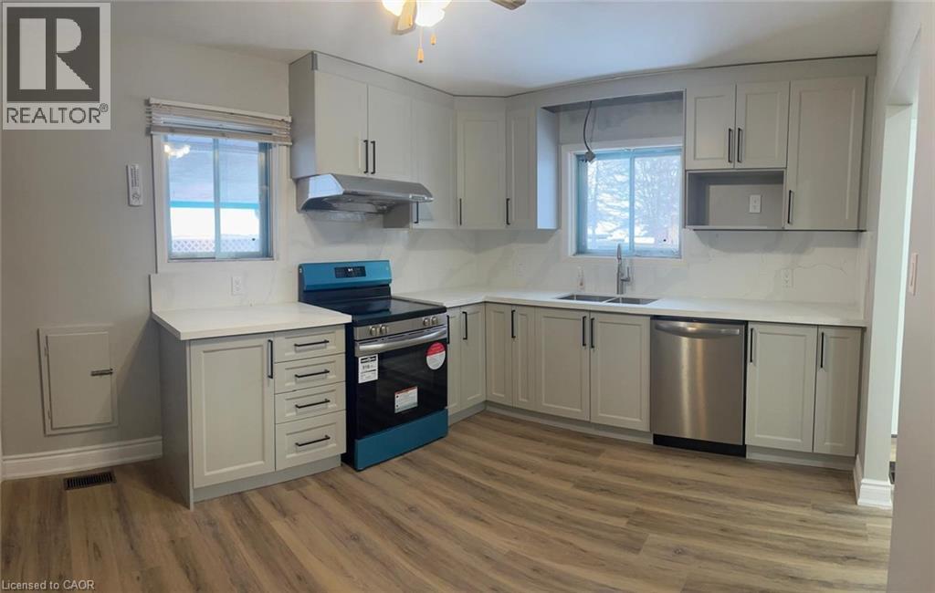 Contemporary kitchen featuring light gray shaker-style cabinetry, white countertops, stainless steel appliances, a stainless steel range hood, and wood-finish flooring - 102 Massey Avenue, Kitchener, ON