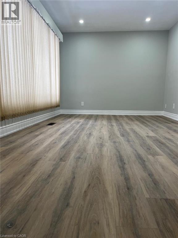 Spacious room featuring wood-finish flooring, light gray wall paint, and recessed ceiling lighting - 102 Massey Avenue, Kitchener, ON