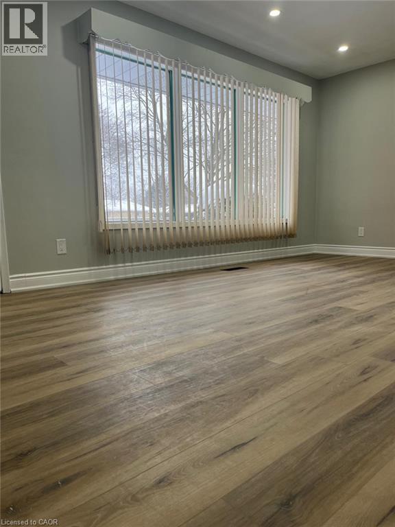 Wood-finish flooring throughout, featuring a large window with vertical blinds, recessed lighting, and crisp white baseboards - 102 Massey Avenue, Kitchener, ON