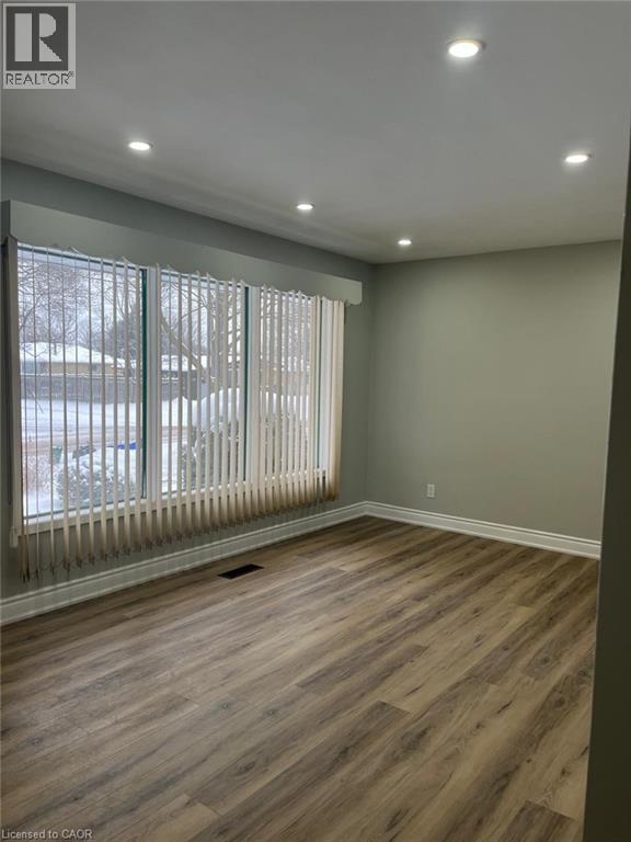 Spacious room featuring wood-finish flooring, recessed ceiling lighting, and a large window with vertical blinds - 102 Massey Avenue, Kitchener, ON