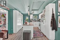 Kitchen featuring a beadboard ceiling in a vibrant hue, wood-finish flooring, white cabinetry, a central island with countertop, and white appliances -
