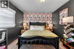 Bedroom featuring a floral accent wall, dark painted walls, wood-finish flooring, and a ceiling-mounted light fixture -