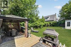 Expansive backyard featuring a large wooden deck with a covered gazebo, a lush green lawn, mature perimeter landscaping, and a detached storage shed -