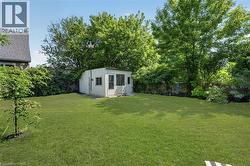 Expansive green lawn with mature trees and a detached shed featuring a single door and multiple windows -