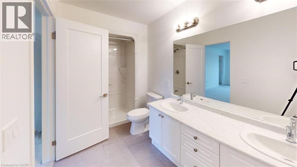 Bathroom featuring a double vanity with two undermount sinks, a long wall-mounted mirror, brushed nickel light fixtures, a toilet, and a stand-up shower with a single-handle faucet - 287 Rockledge Drive, Hamilton, ON