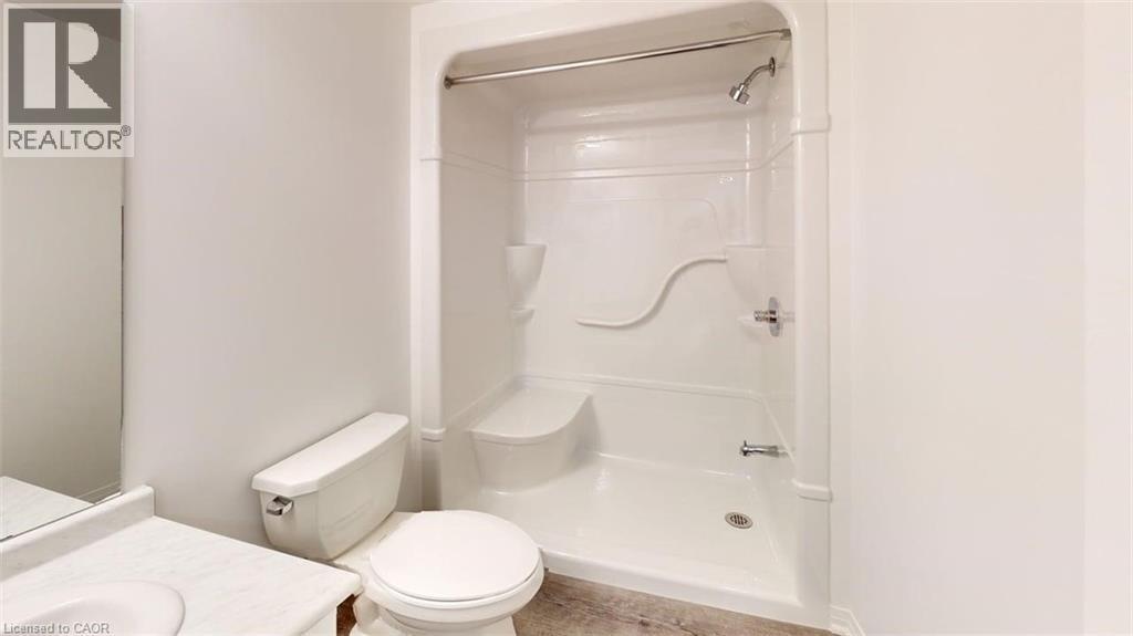 Bathroom featuring a white integrated tub and shower unit, a white toilet, and a vanity with an integrated sink and light-colored countertop - 287 Rockledge Drive, Hamilton, ON