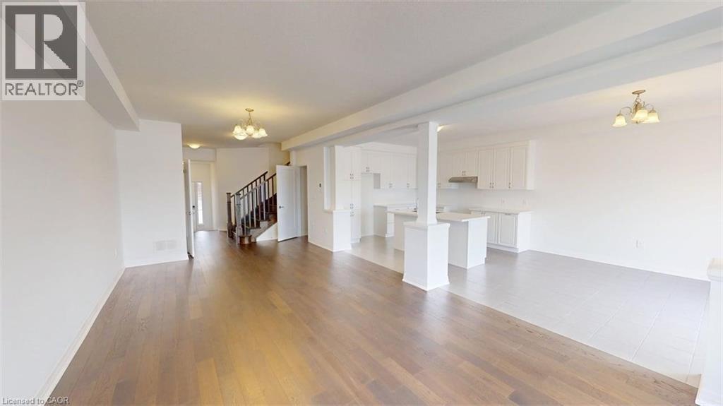 Spacious open-concept living area featuring wood-finish flooring, a white kitchen with upper and lower cabinetry, a kitchen island, and a staircase with dark wood-finish banister - 287 Rockledge Drive, Hamilton, ON