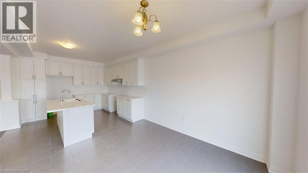 Kitchen featuring white cabinetry, a center island with an undermount sink and gooseneck faucet, light countertops, and grey tile flooring - 287 Rockledge Drive, Hamilton, ON