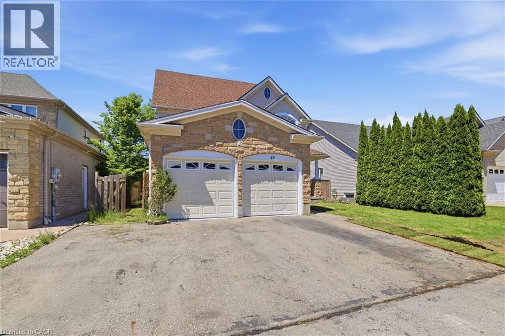 Stone facade residence featuring a two-car garage with arched entrances, a red shingled roof, and an oval window accent - 43 Decaro Crescent, Cambridge, ON