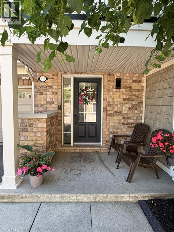 Inviting covered porch entry featuring brick facade, a dark paneled door with window inserts, and sconce lighting - 7 Sirente Drive Unit# 11, Hamilton, ON - Outdoor