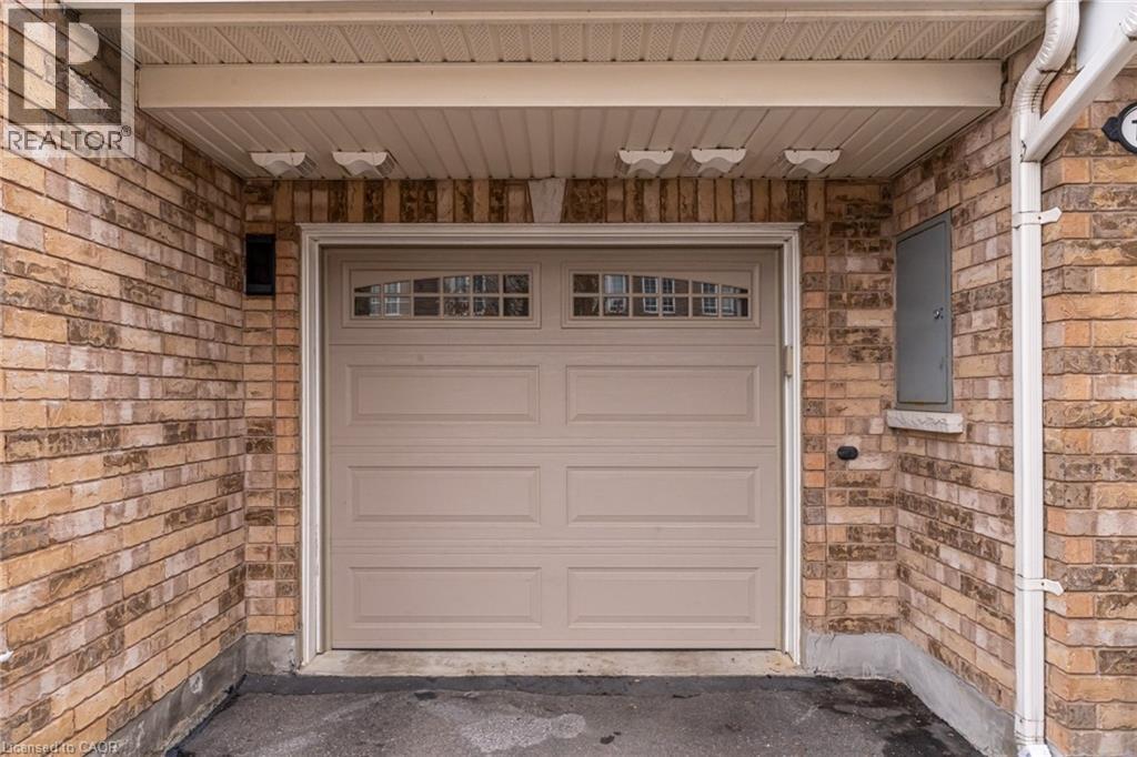 Brick exterior featuring a paneled garage door with upper window inserts, an overhead soffit, and exterior lighting fixtures - 7 Sirente Drive Unit# 11, Hamilton, ON - Outdoor With Exterior