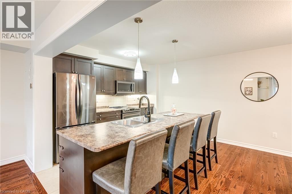 Open-concept kitchen featuring dark wood cabinetry, stainless steel appliances, and a light-toned backsplash - 7 Sirente Drive Unit# 11, Hamilton, ON - Indoor Photo Showing Other Room