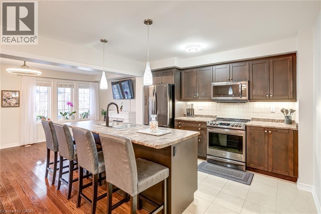 Kitchen featuring a large island with sink, ample dark wood cabinetry, stainless steel appliances, and light-colored countertops - 7 Sirente Drive Unit# 11, Hamilton, ON - Indoor Photo Showing Kitchen With Upgraded Kitchen