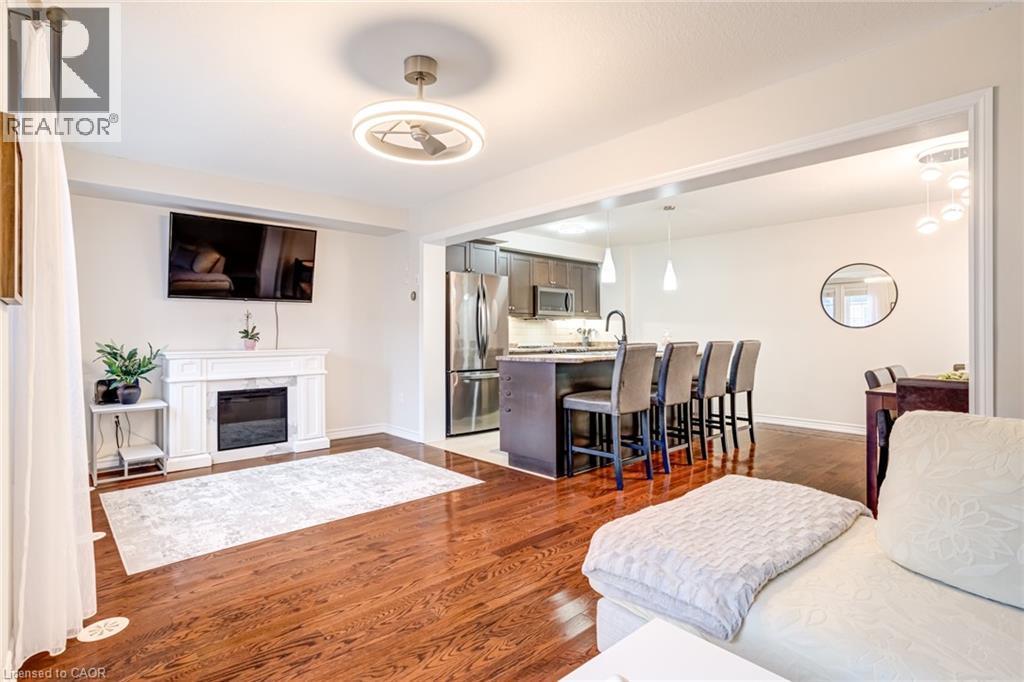 Open concept living space featuring rich wood-finish flooring, a decorative fireplace with a white mantel, and a ceiling fan with integrated lighting - 7 Sirente Drive Unit# 11, Hamilton, ON - Indoor With Fireplace