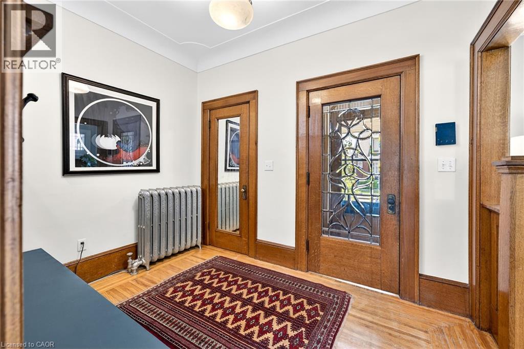 Entryway featuring a wood-finish door with leaded glass, hardwood flooring, detailed baseboards, and a classic radiator - 22 Connaught Avenue S, Hamilton, ON