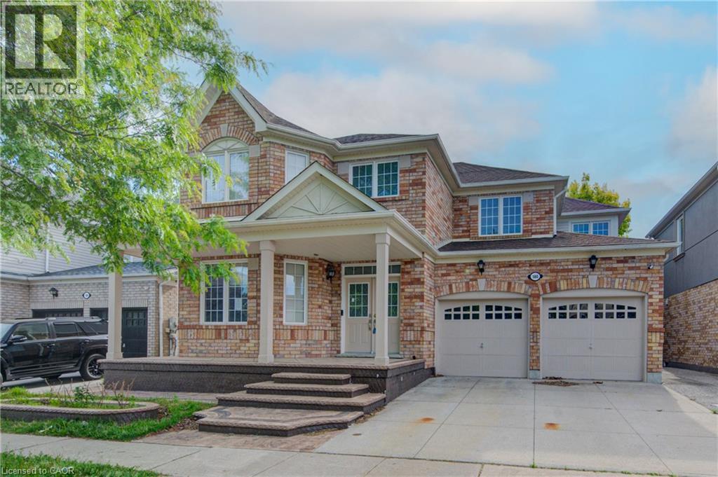 Brick exterior featuring a covered porch with white columns, a two-car garage, and multiple large windows - 180 Arthur Fach Drive, Cambridge, ON