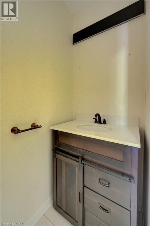 Modern vanity featuring a white countertop, undermount sink, and dark wood-finish cabinetry with barn door hardware - 180 Arthur Fach Drive, Cambridge, ON