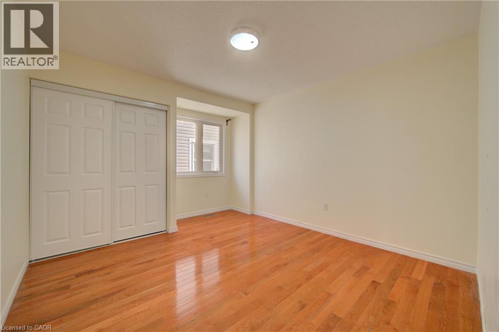 Room featuring warm wood-finish flooring, a white bi-fold closet, a double window, and light-toned walls - 180 Arthur Fach Drive, Cambridge, ON
