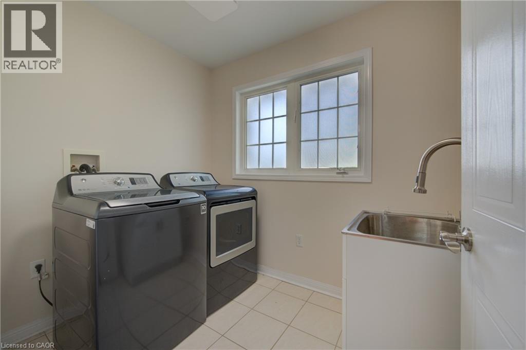 Dedicated laundry space featuring a utility sink with a high-arc faucet, tiled flooring, and a large window with grid panes - 180 Arthur Fach Drive, Cambridge, ON