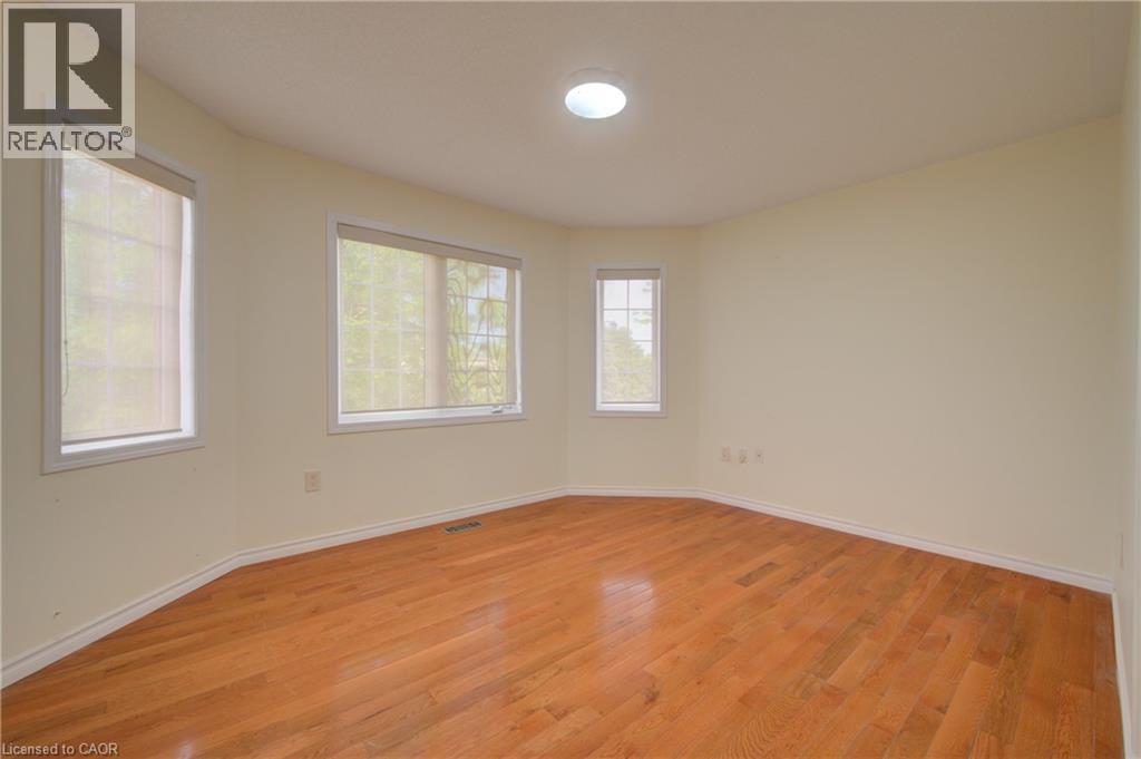 Spacious room featuring wood-finish flooring, multiple windows with roller shades, a flush-mount ceiling light, and neutral wall tones - 180 Arthur Fach Drive, Cambridge, ON