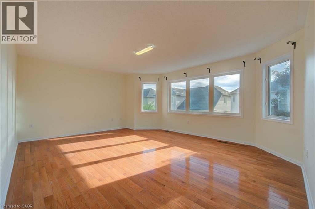 Spacious room featuring wood-finish flooring, a curved wall, and a bay window configuration with multiple windows - 180 Arthur Fach Drive, Cambridge, ON
