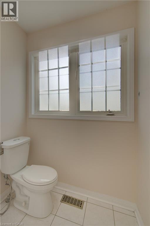 White ceramic toilet with a dual-pane window featuring grid patterns, white trim, and frosted glass - 180 Arthur Fach Drive, Cambridge, ON