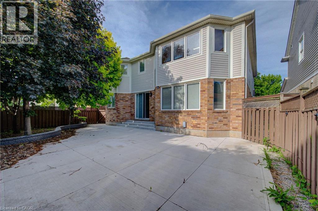 Rear exterior featuring a spacious concrete patio, brick and siding facade, multiple windows, and a sliding glass door - 180 Arthur Fach Drive, Cambridge, ON