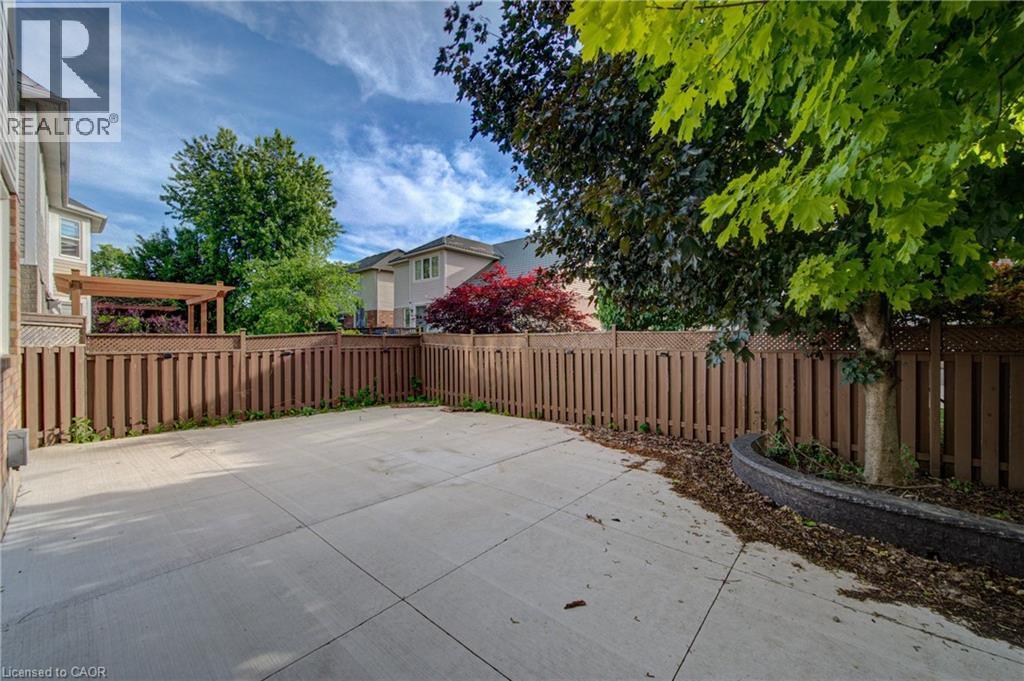 Paved patio area featuring a wooden privacy fence, mature trees, and a built-in planter with stone detailing - 180 Arthur Fach Drive, Cambridge, ON