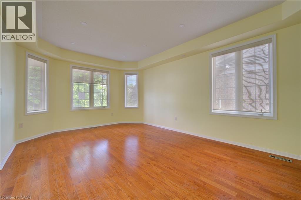 Expansive room featuring rich wood-finish flooring, a tray ceiling, and multiple windows with roller shades - 180 Arthur Fach Drive, Cambridge, ON