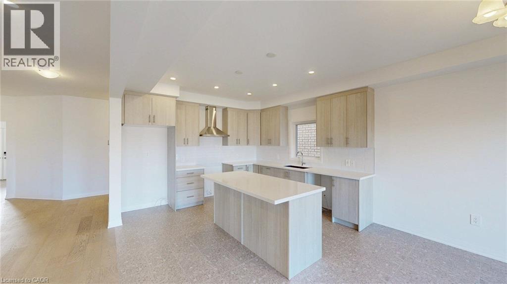 Modern kitchen featuring light wood-finish cabinetry, a large center island with a light-toned countertop, and a stainless steel range hood - 200 Cittadella Boulevard, Hamilton, ON