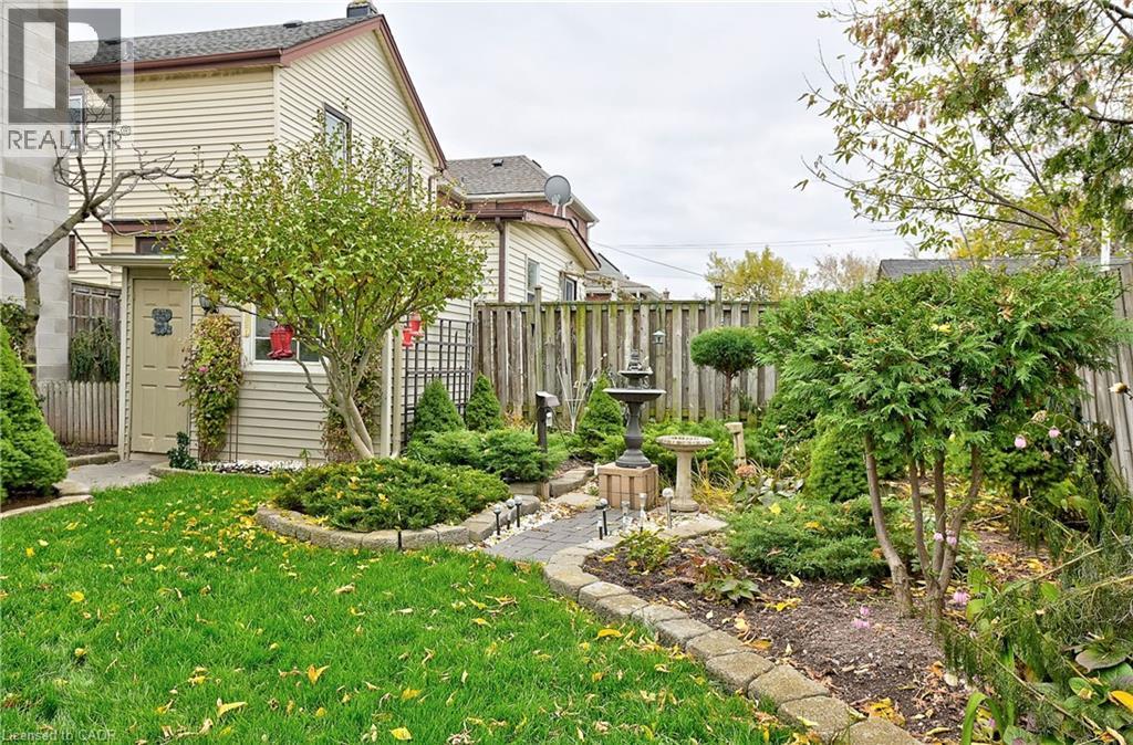 Landscaped backyard featuring a stone-lined garden path, mature shrubs, a decorative fountain, a privacy fence, and a manicured lawn - 1476 Barton Street E Unit# 2, Hamilton, ON