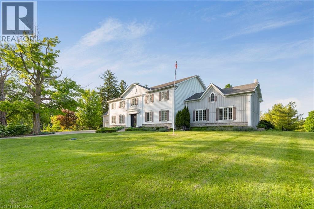 Expansive green lawn with mature trees framing a traditional-style property featuring white siding and dark shutters - 6195 Milburough Line, Burlington, ON - Outdoor