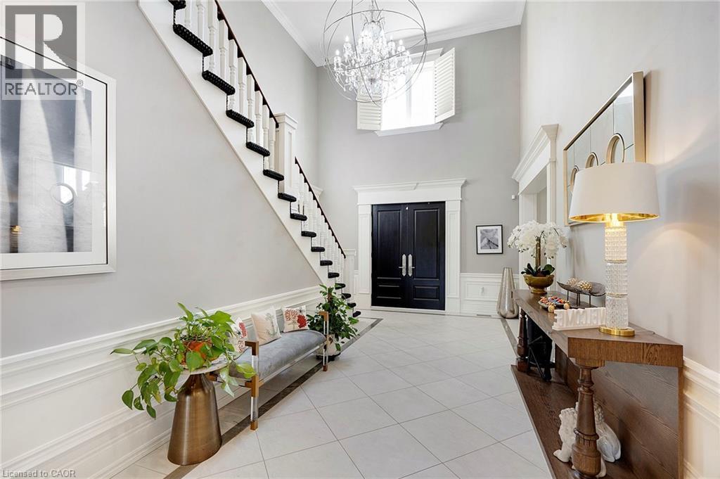 Two-story foyer featuring a grand staircase with dark treads and white risers, double entry doors, a large chandelier, and wainscoting - 6195 Milburough Line, Burlington, ON - Indoor Photo Showing Other Room