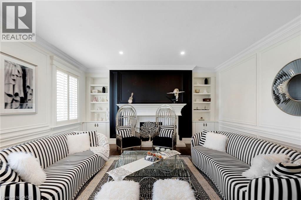 Living room featuring an ornate fireplace with a black accent wall, symmetrical built-in shelving, crown molding, recessed lighting, and wall paneling - 6195 Milburough Line, Burlington, ON - Indoor