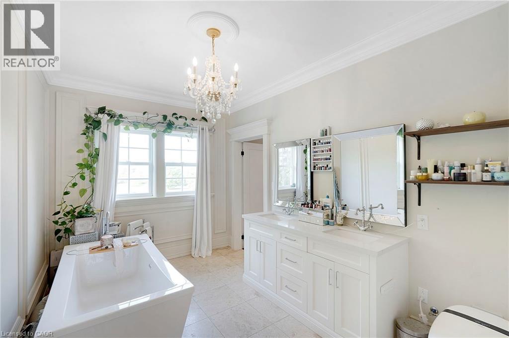 Bright bathroom featuring a freestanding tub, double vanity with integrated sinks, and a crystal chandelier - 6195 Milburough Line, Burlington, ON - Indoor Photo Showing Bathroom