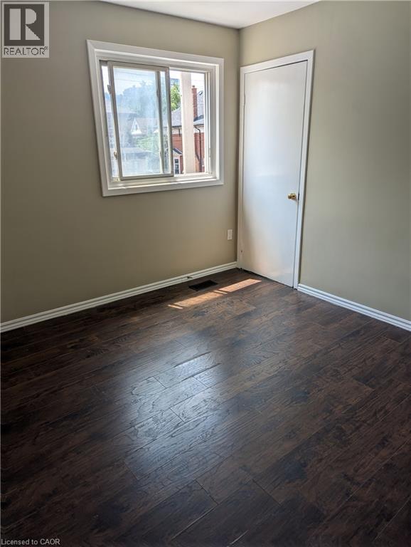 Room featuring dark wood-finish flooring, light tan walls, and white baseboards - 949 E Main Street E, Hamilton, ON