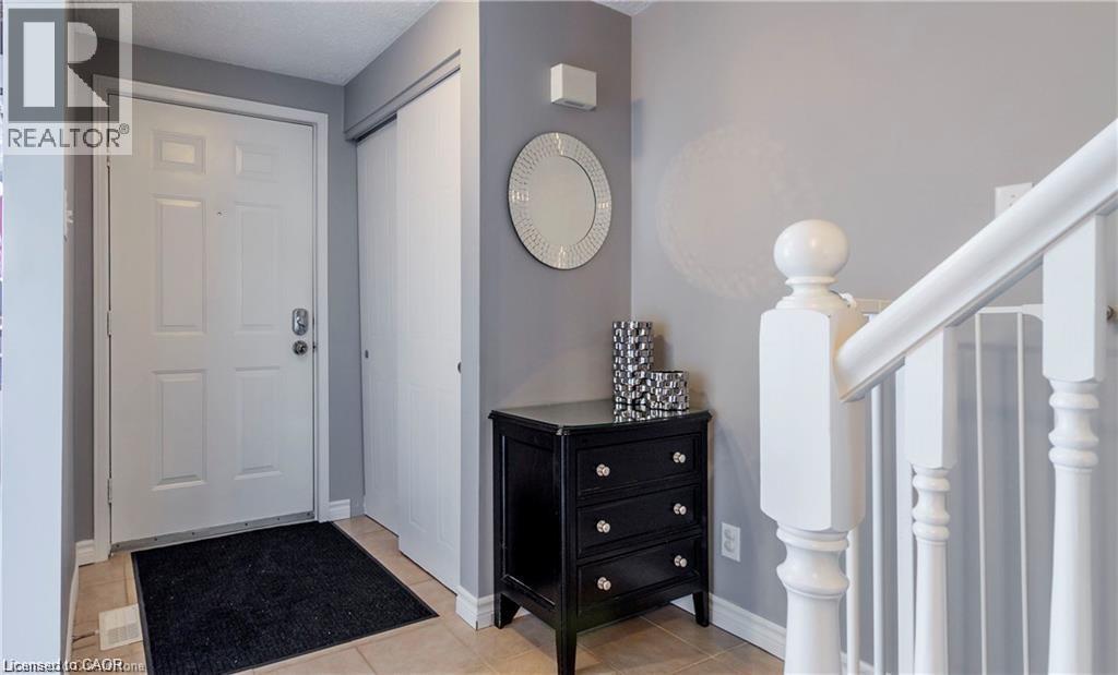 Foyer with light-toned tile flooring, a paneled entry door, and an adjacent closet with white sliding doors - 209 Auburn Drive Unit# A, Waterloo, ON