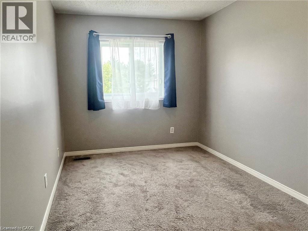 Room featuring neutral wall tones, textured carpeting, and a window with natural light - 209 Auburn Drive Unit# A, Waterloo, ON