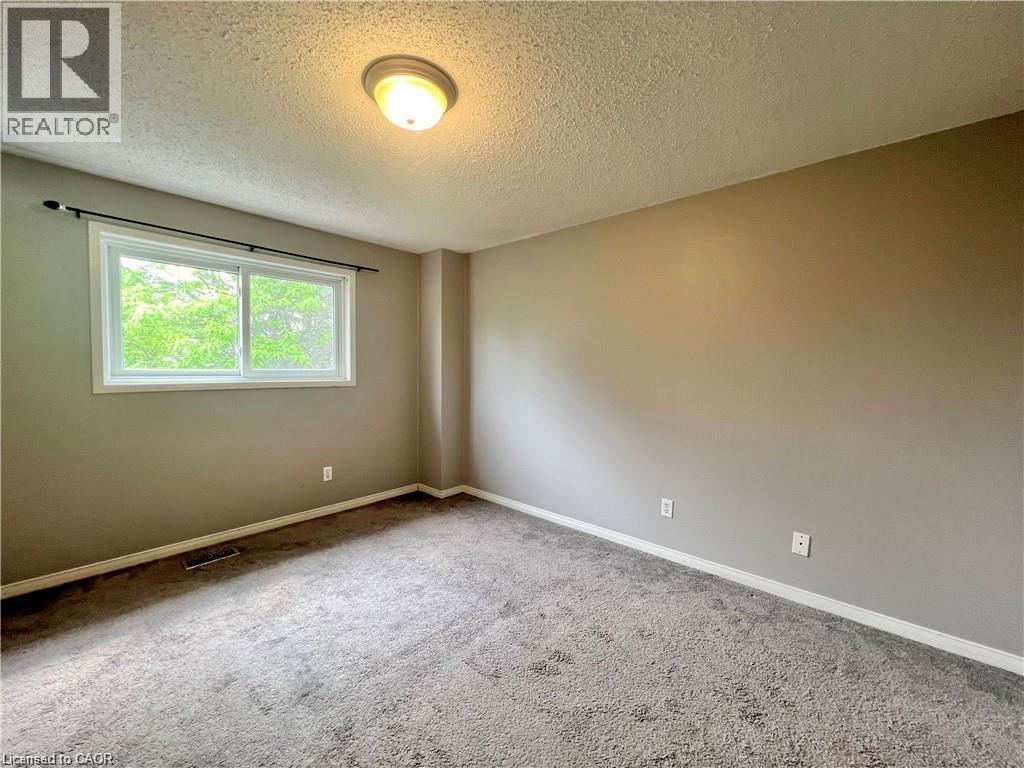 Carpeted room featuring a white-trimmed window, neutral wall paint, white baseboards, a flush-mount ceiling light fixture, and a dark curtain rod - 209 Auburn Drive Unit# A, Waterloo, ON