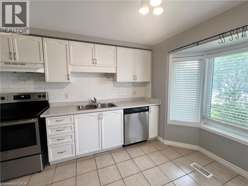 Kitchen featuring white cabinetry, subway tile backsplash, stainless steel appliances, a double basin sink, and a bay window - 209 Auburn Drive Unit# A, Waterloo, ON