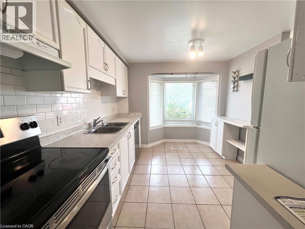 Kitchen featuring white cabinetry, subway tile backsplash, stainless steel range, dual basin sink, and a bay window with blinds - 209 Auburn Drive Unit# A, Waterloo, ON