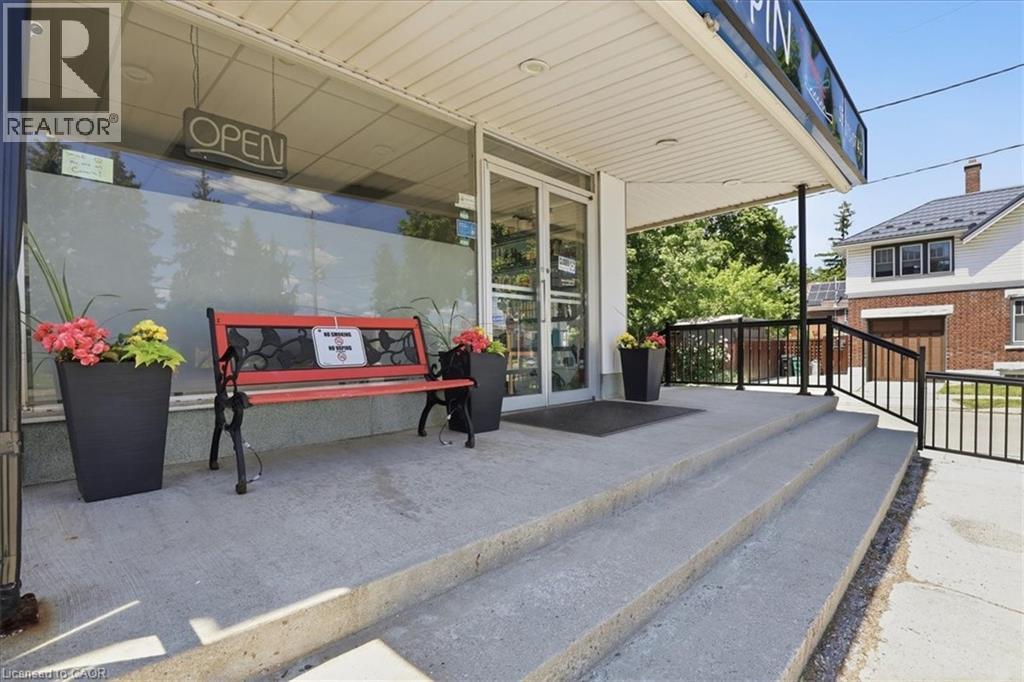 Commercial storefront featuring a wide concrete entrance, large display windows, and a covered porch area - 744 Queen Street S, Kitchener, ON