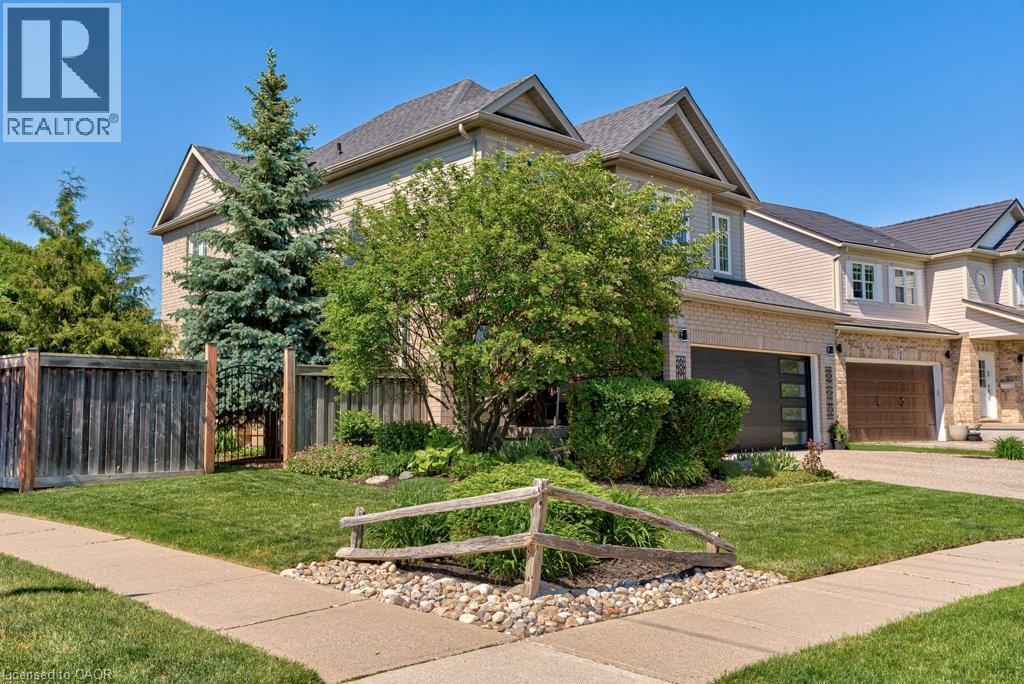 Exterior featuring light-toned siding and brick accents, a dark shingled roof, an attached garage with a modern dark door, a concrete sidewalk, and established landscaping with mature trees and shrubs - 61 Ditner Avenue, Baden, ON - Outdoor