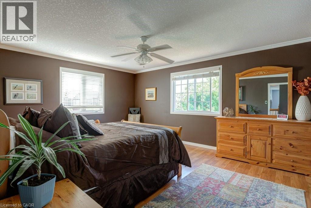Bedroom featuring wood-finish flooring, two large windows, a ceiling fan, crown molding, and a warm brown wall color - 61 Ditner Avenue, Baden, ON - Indoor Photo Showing Bedroom