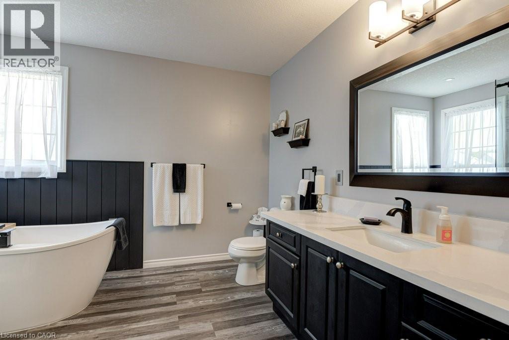 Bathroom featuring a freestanding tub, wood-finish flooring, a double vanity with a light-colored countertop, dark wood cabinetry, and a framed mirror - 61 Ditner Avenue, Baden, ON - Indoor Photo Showing Bathroom