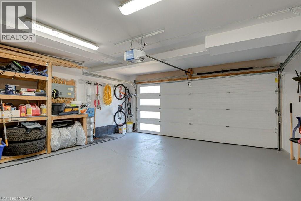 Spacious garage featuring a modern overhead door with frosted glass panels, painted concrete flooring, and built-in wooden shelving for organization - 61 Ditner Avenue, Baden, ON - Indoor Photo Showing Garage