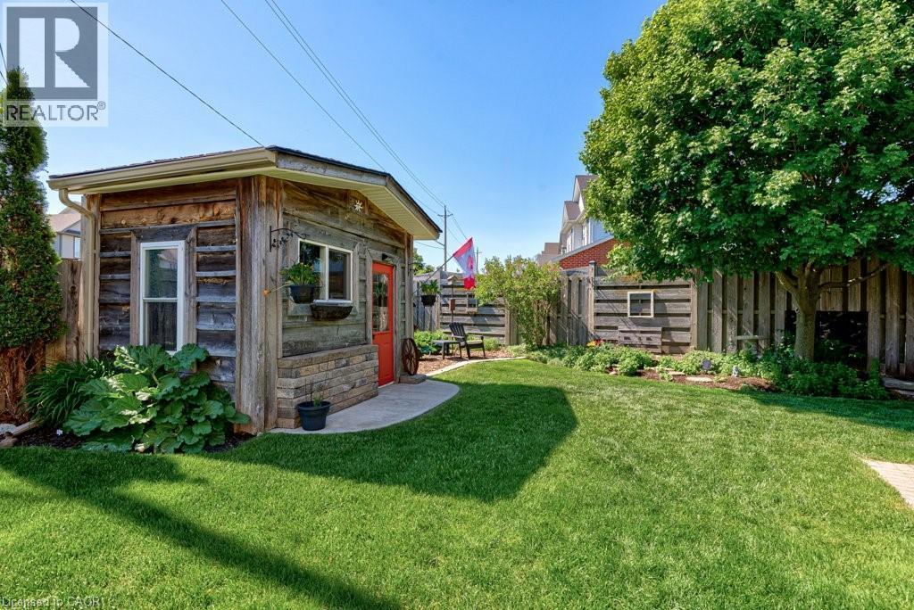 Backyard featuring a shed with wood-finish siding, a bright red entry door, multiple windows, and an adjacent curved concrete patio - 61 Ditner Avenue, Baden, ON - Outdoor