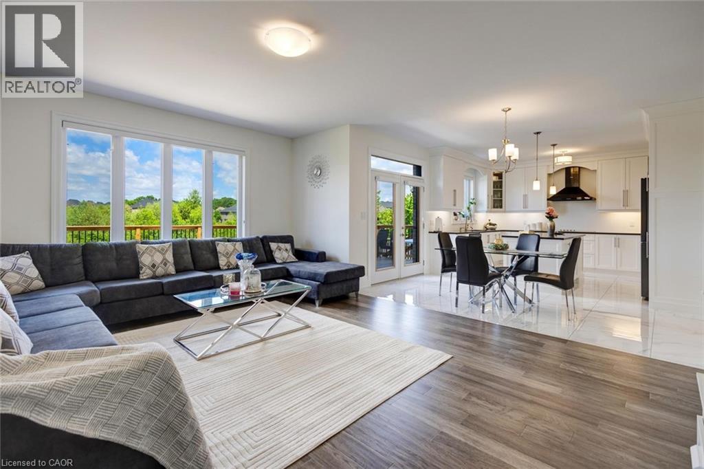Open-concept living area featuring wood-finish flooring, large windows, and a glass-paneled door - 57 Hollybrook Trail, Kitchener, ON